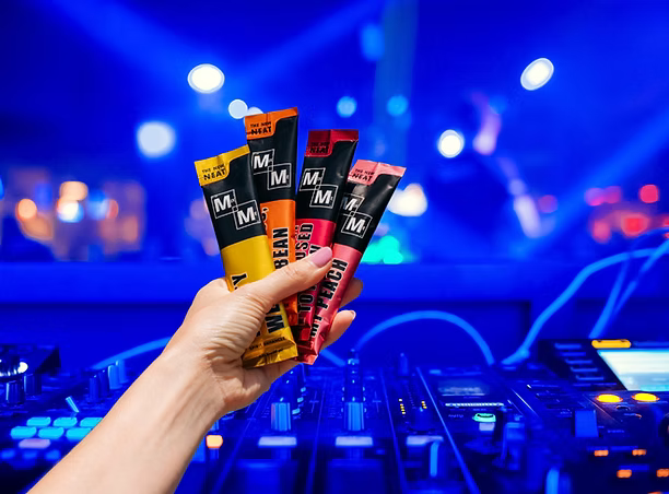 Hand holding Mixmeco cocktail mixers with a colorful, blurred background